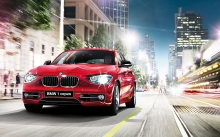 Блестящий красный BMW 1 series на главной улице вечернего мегаполиса